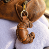 Leather croissant bag charm with gold clasp attached to brown handbag