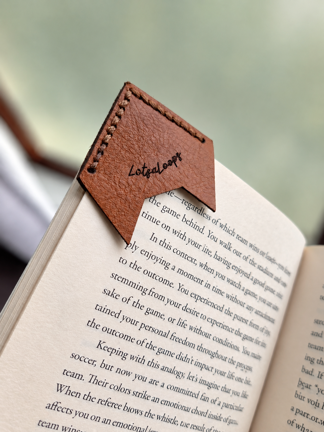 Back of leather fox corner bookmark on a book page showing the LotsaLoops logo