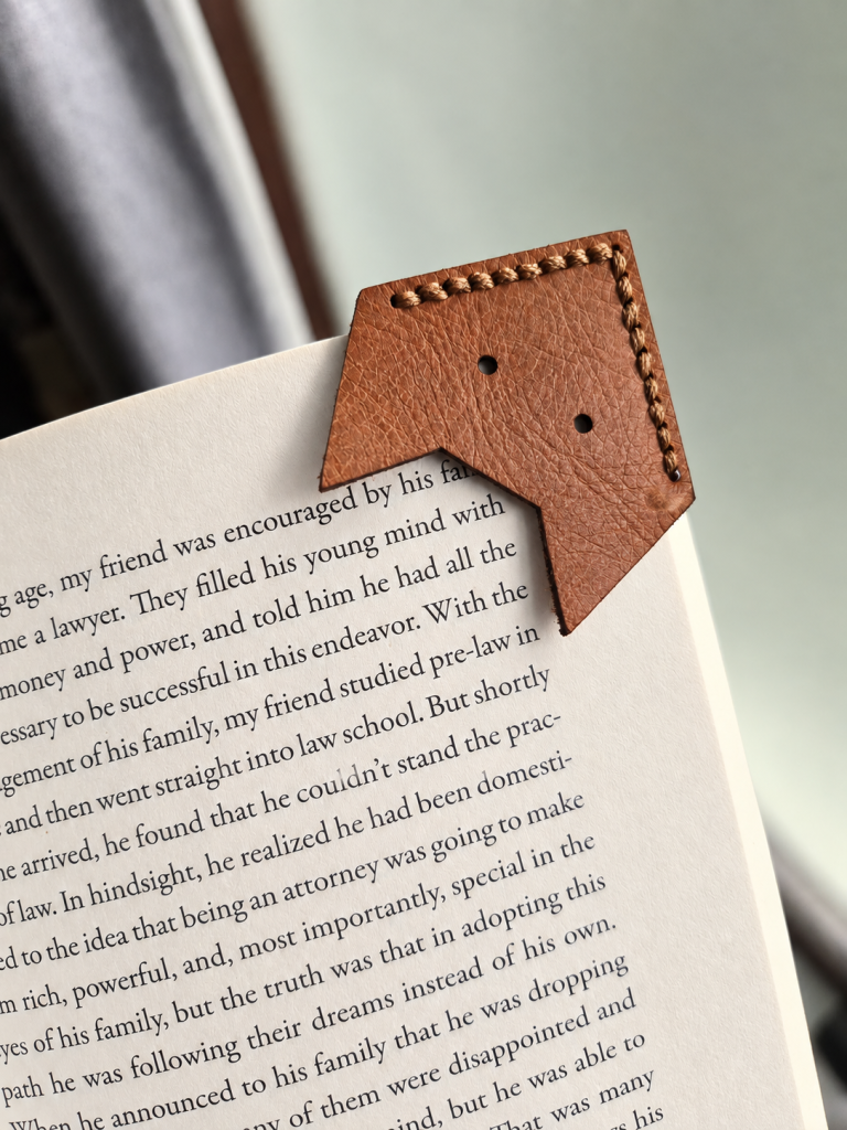 Front of leather fox corner bookmark on a book page showing the cut-out fox face and hand stitching