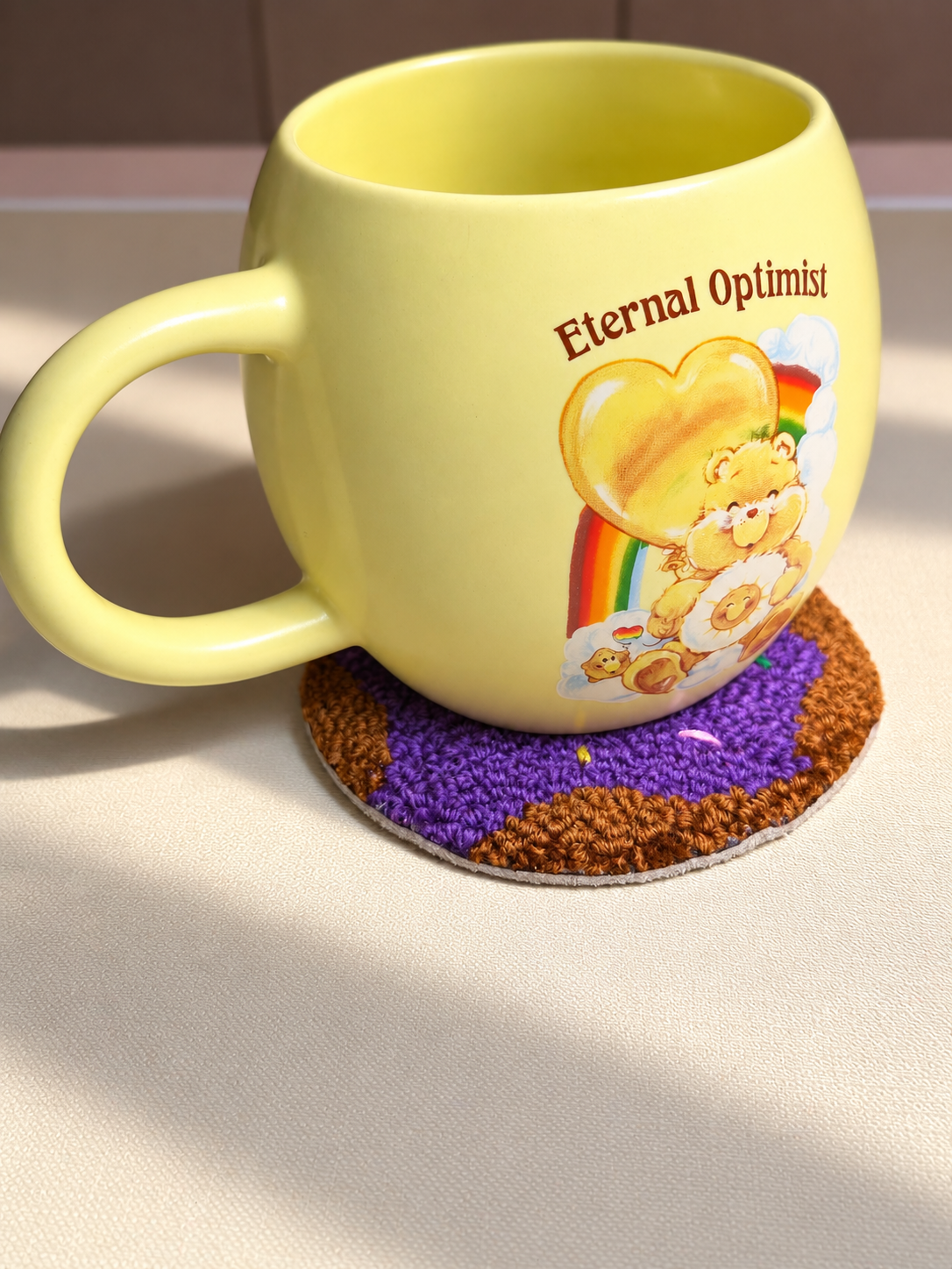 Purple donut punch needle mug rug underneath a yellow mug