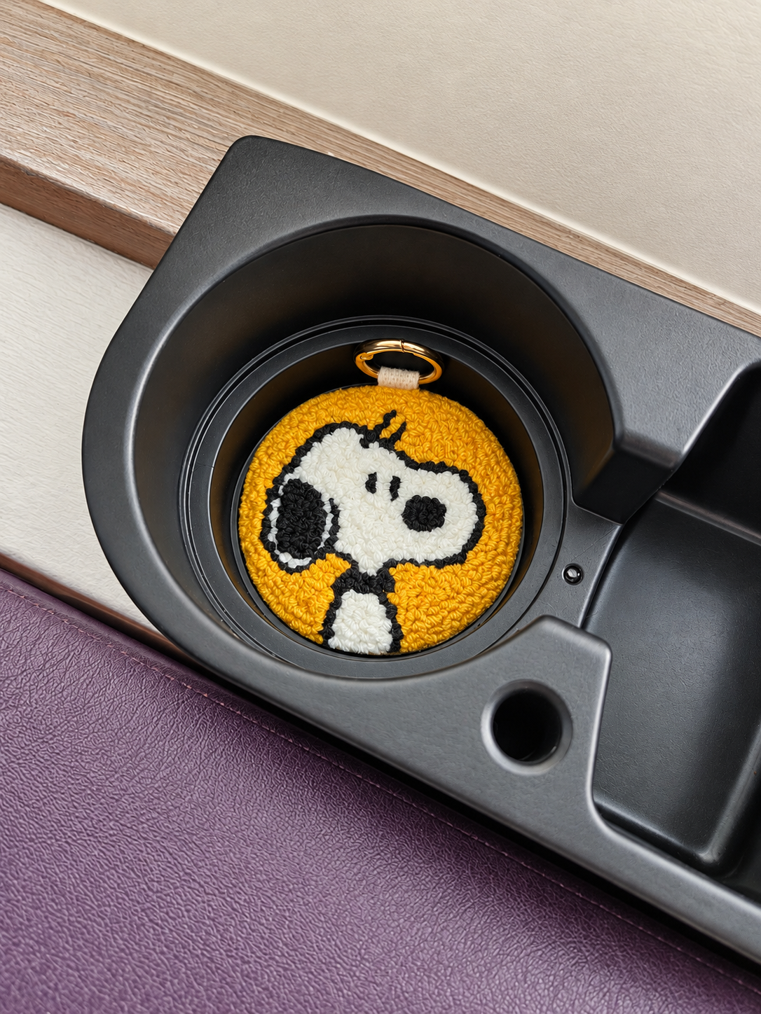 Mustard-yellow Snoopy punch needle coaster with genuine leather backing, placed inside a car cup holder.