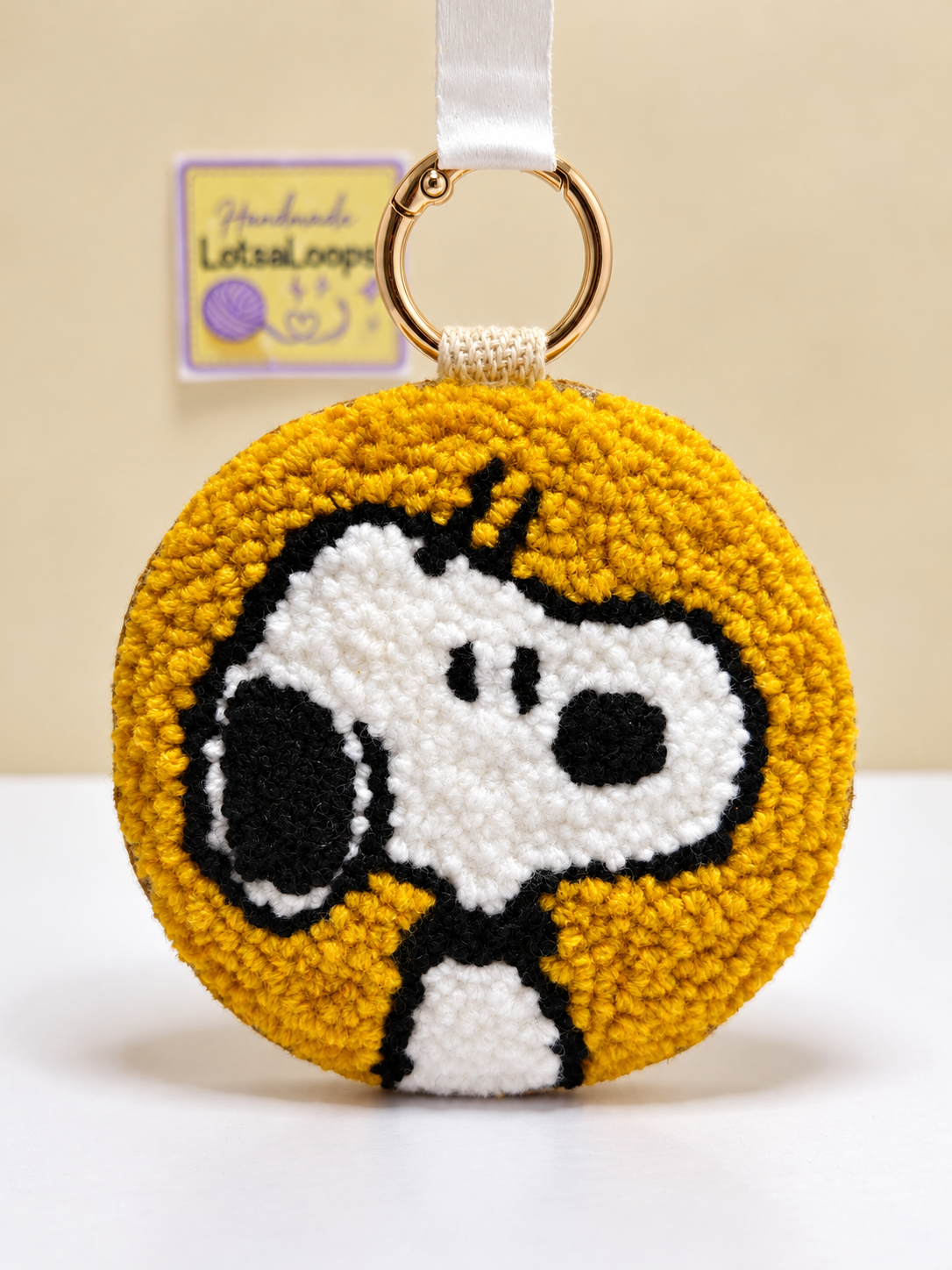 Front view of handmade Snoopy punch needle 2-in-1 accessory with mustard-yellow background, black and white detailing and gold clasp.